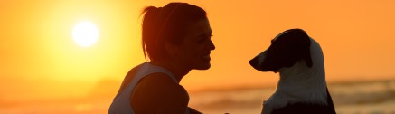 Frau mit Hund am Strand bei Sonnenuntergang